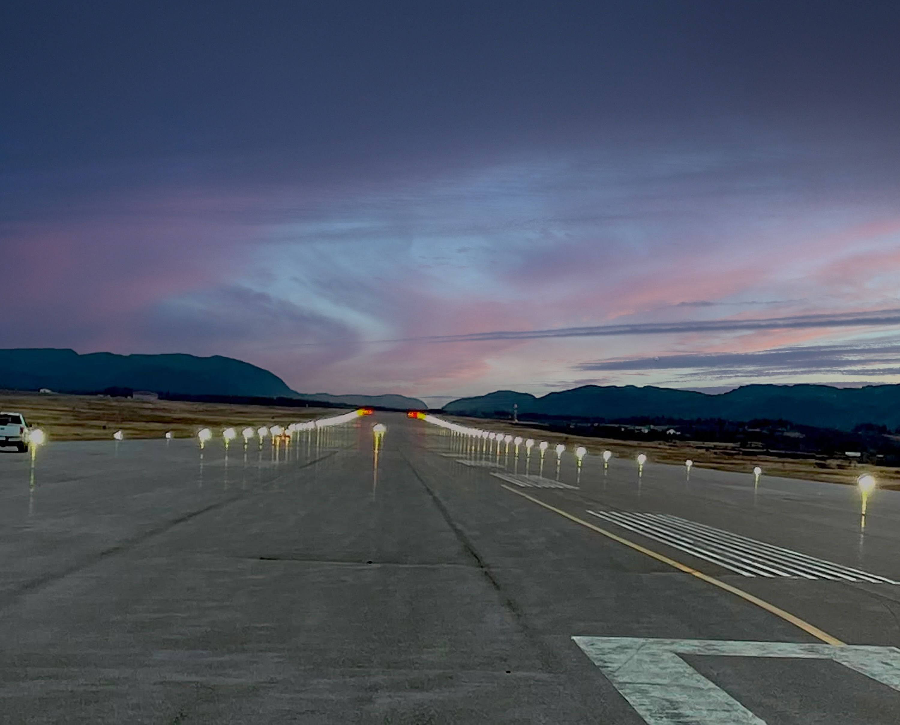 The runway at Stephenville International Airport at dusk, edge lights on, with the Long Range Mountains beyond.